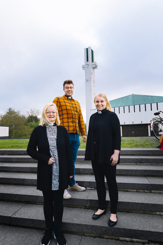 Kuvassa kolme pappia seisomassa portailla Lakeuden Risti -kirkon edustalla.